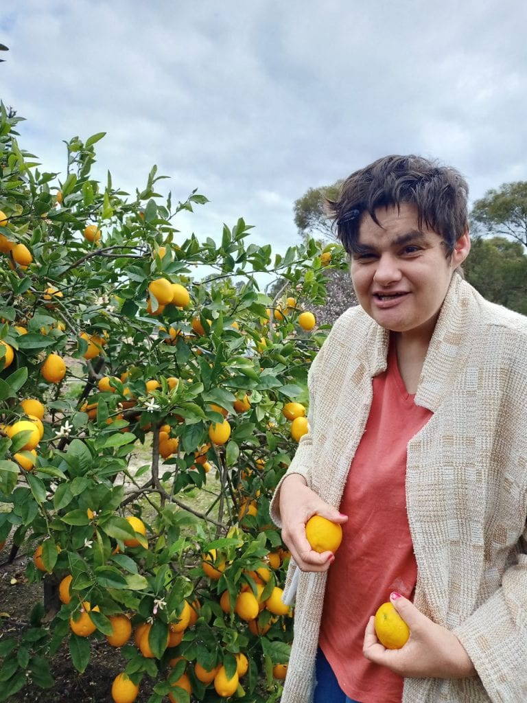 a woman standing in front of a tree holding two oranges