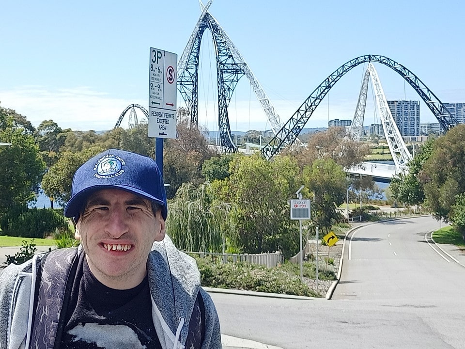 a man wearing a blue hat and jacket standing in front of a roller coaster