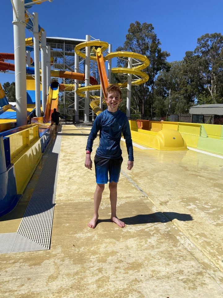 a young boy standing in front of a water slide