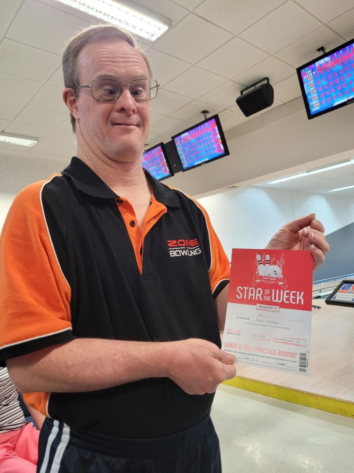a man holding up a certificate in a bowling alley
