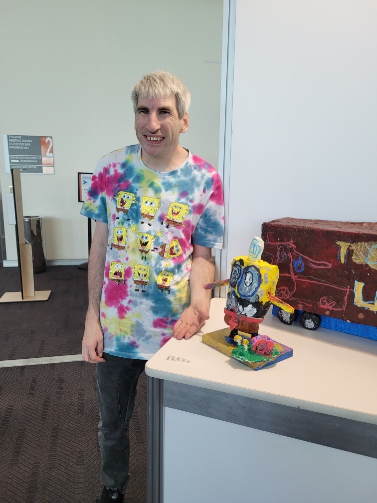 a man in a tie - dyed shirt standing next to a toy train