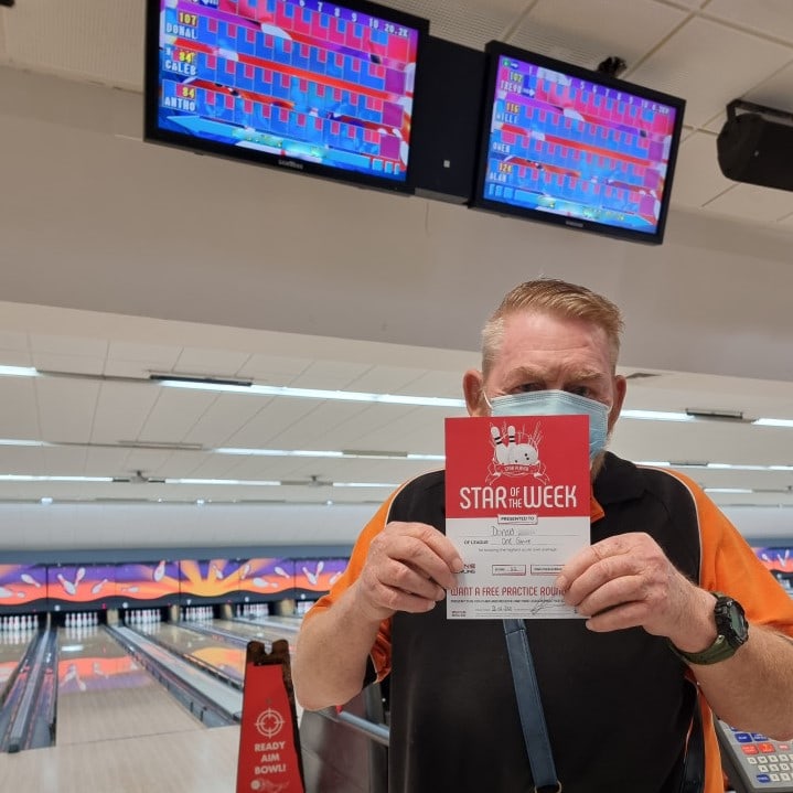 a man holding up a sign in front of bowling lanes