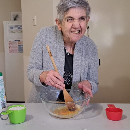 an older woman mixing a bowl of food with a wooden spoon