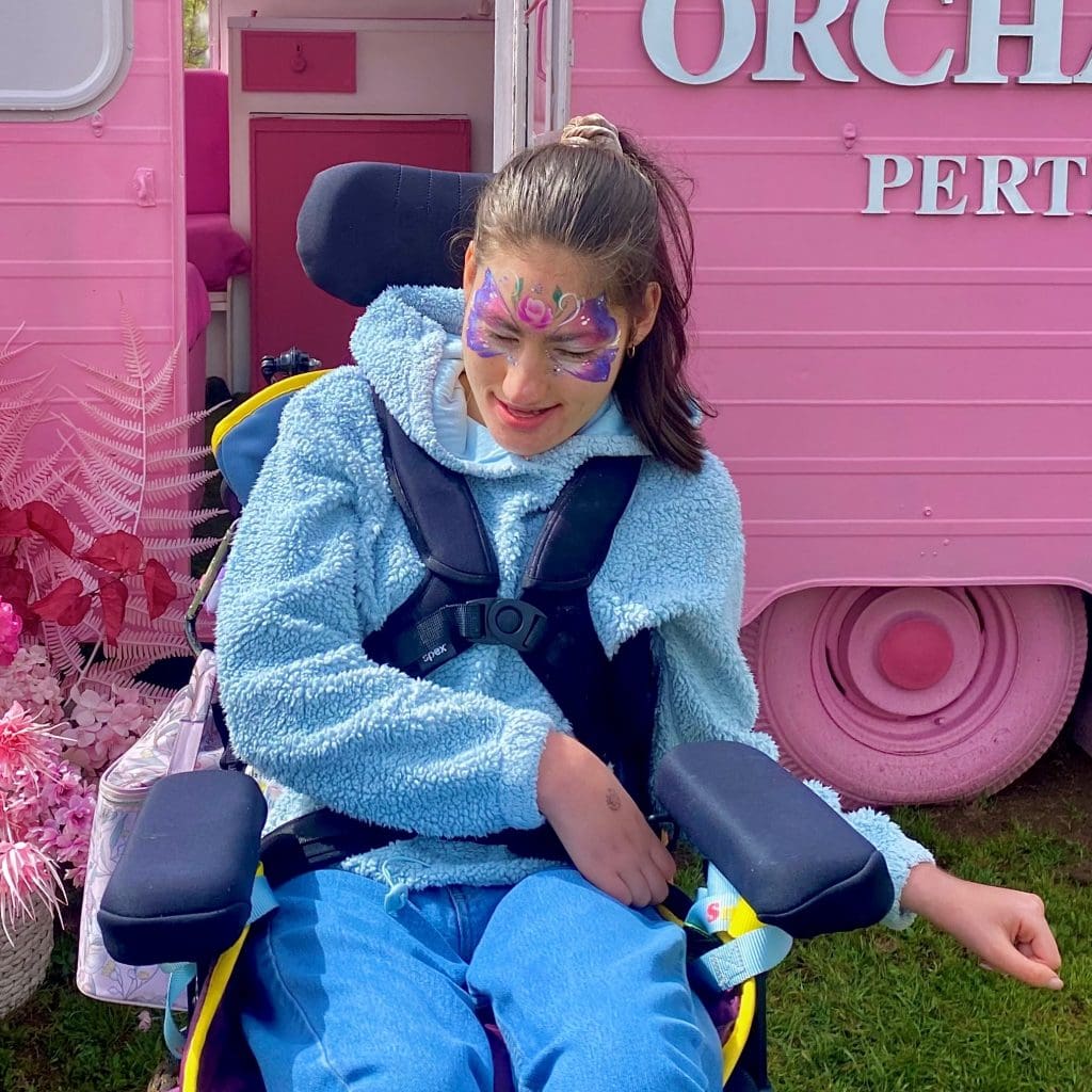 a little girl sitting in a wheel chair in front of a pink bus