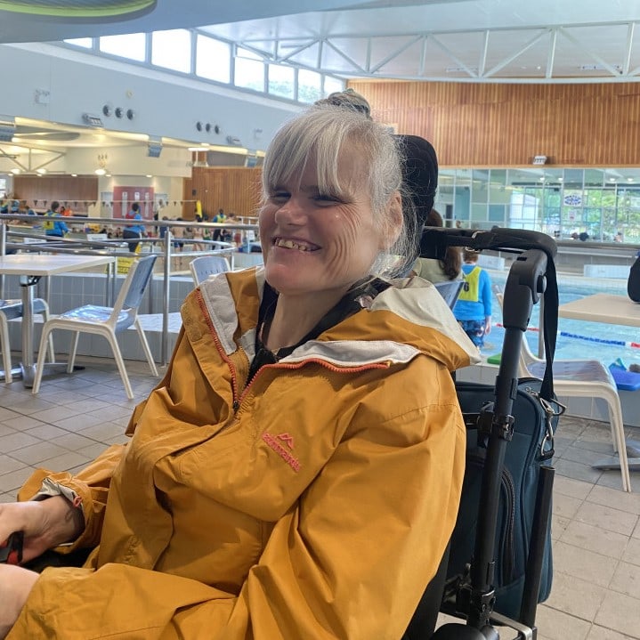 a woman in a yellow jacket sitting in a wheel chair and smiling.