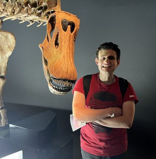 a man standing in front of a fake dinosaur head