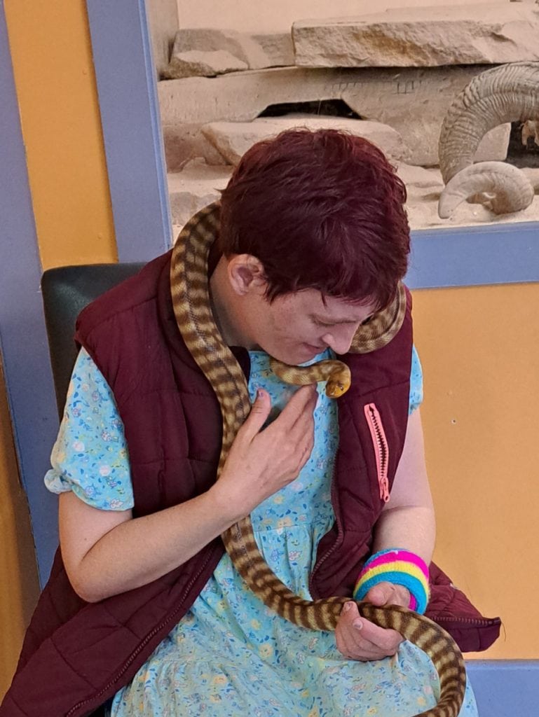 a woman sitting down with a snake wrapped around her neck