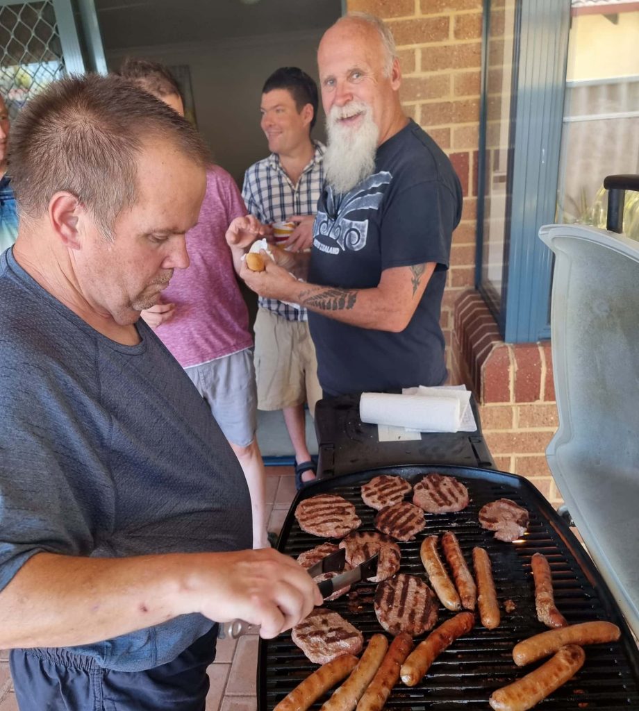 a man is grilling hot dogs and burger on a grill with his friends