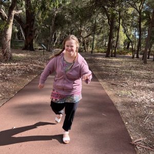 a young girl running down a path in a park.