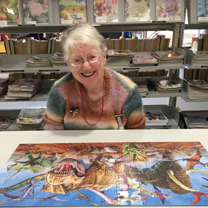 a woman sitting at a table in front of a puzzle.