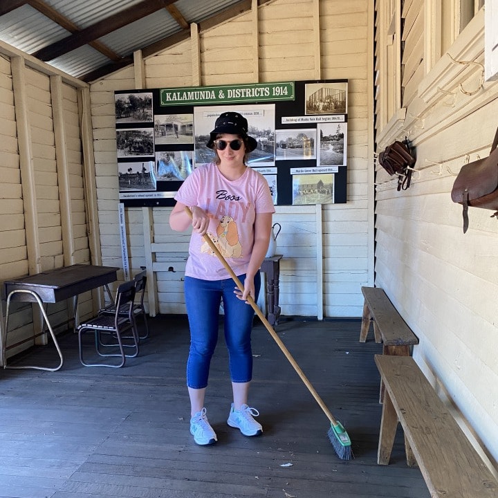 a woman in a pink shirt is holding a broom.