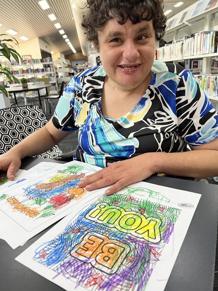 Lady in a library with a completed colouring page that says "be you"
