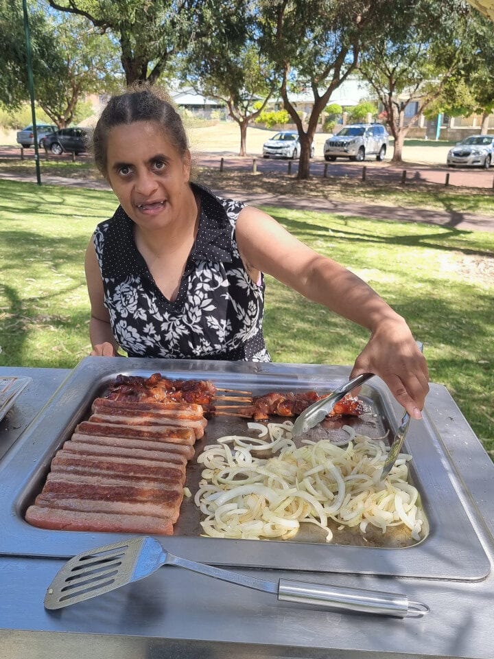 Lady cooking sausages and onions on an outdoor barbecue at the park