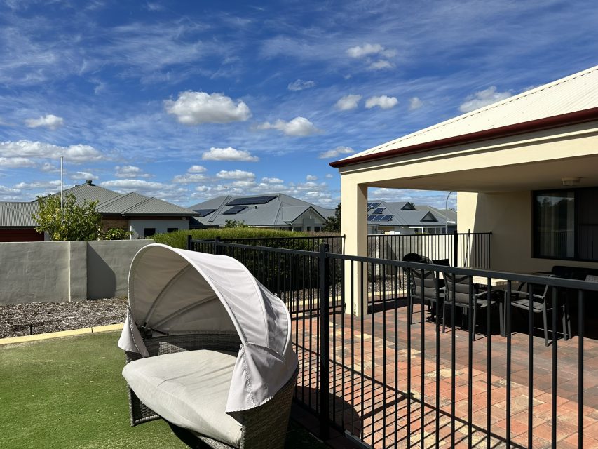 Ooutdoor lounge chair sits on the grass with a dining area under the patio behind.