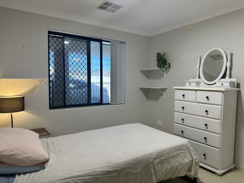 Neutral coloured bedroom with beige and pink bedding and a white chest of drawers.